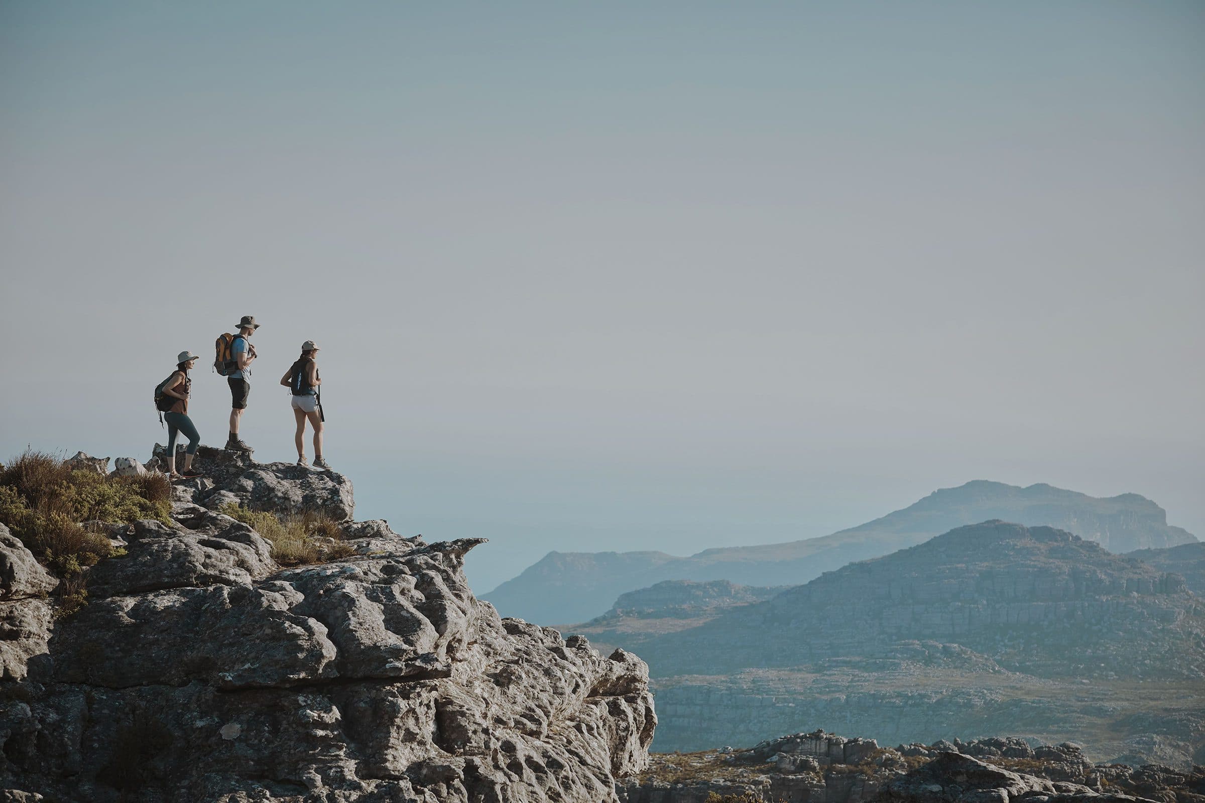 three people standing at the top of a mountain looking at the view