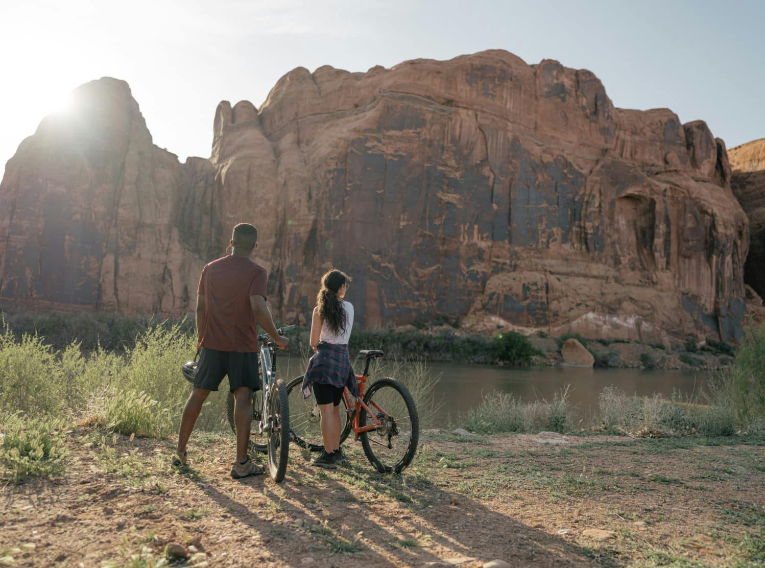 couple with bikes overlooking a river next to red rock cliffs