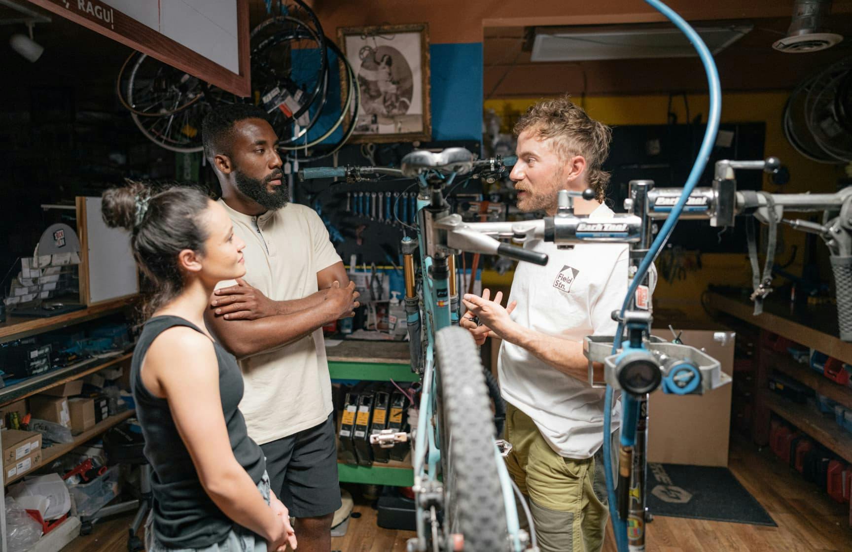 Man and woman in bike shop listening to shopkeeper talk about a bike