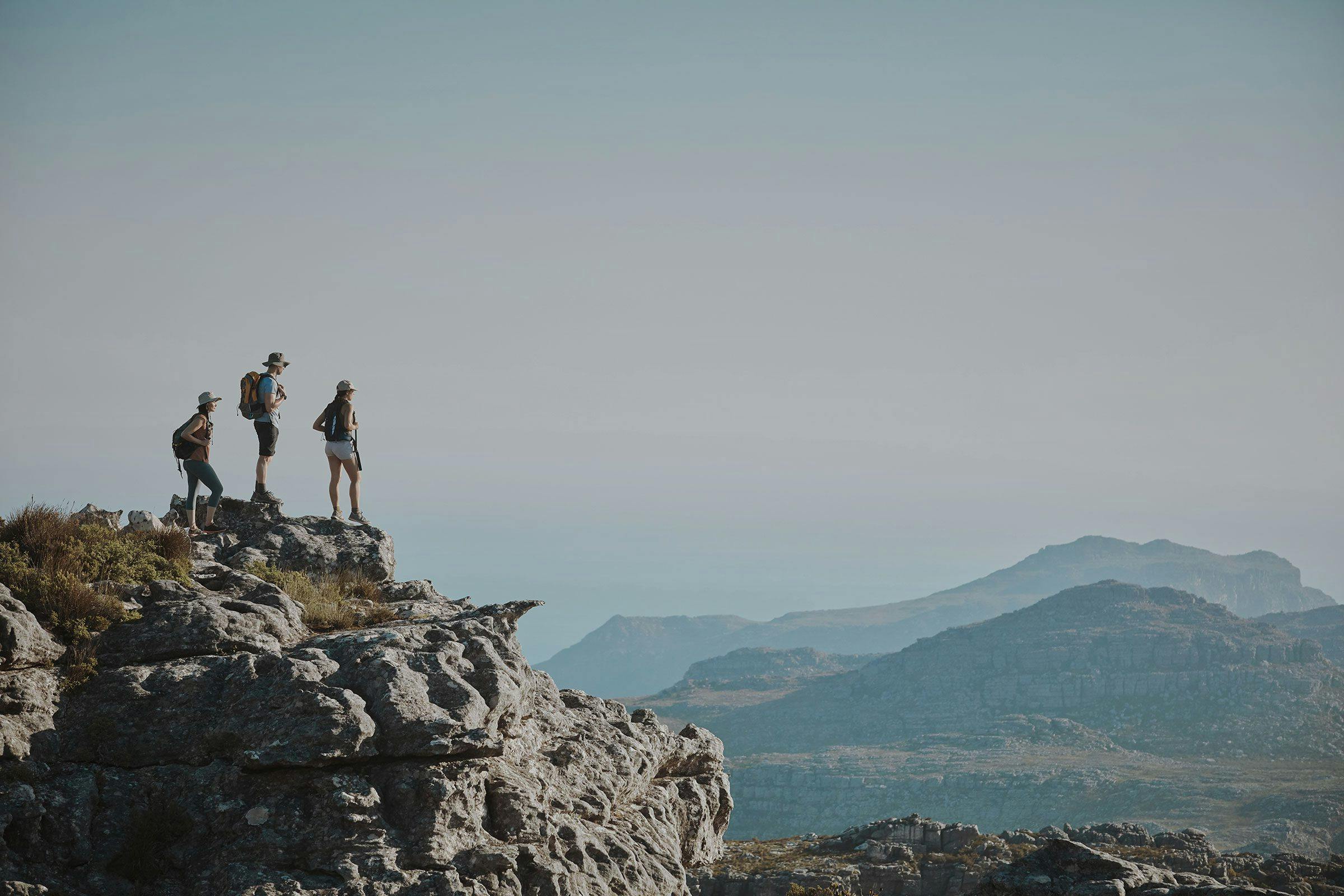 three people standing at the top of a mountain looking at the view