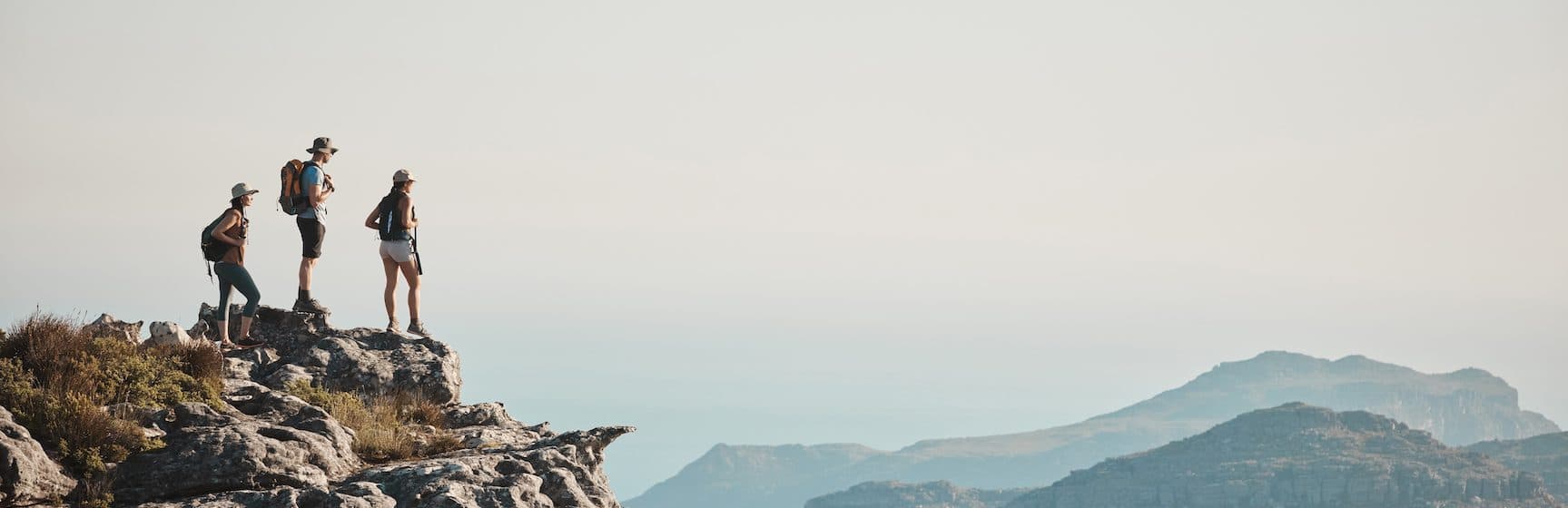 three people standing on a cliff edge overlooking a wilderness vista